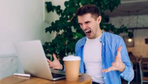 Man looking at laptop and yelling in frustration