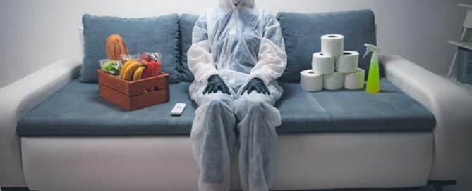 Women in PPE sitting on couch with sanitizer, tissues and produce around her